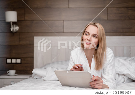 An attractive middle-aged blonde woman in a white bathrobe is lying on a bed in the bedroom and is 55199937