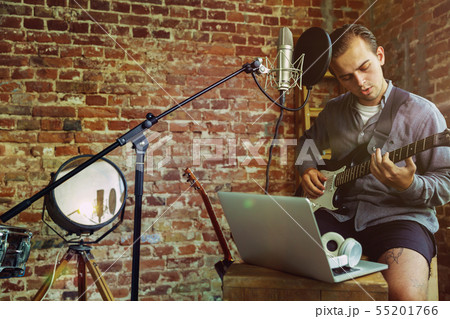 Young man recording music, playing guitar and singing at home Young man recording music, playing guitar and singing at home 55201766