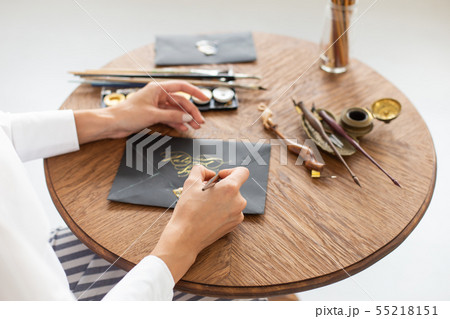Woman calligrapher is holding a pen with ink and signs a card in handwritten font. Close-up. Soft Woman calligrapher is holding a pen with ink and signs a card in handwritten font. Close-up. Soft 55218151