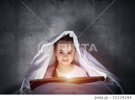 Happy little girl reading book in bed 55229284