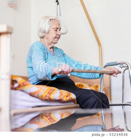 Elderly 96 years old woman exercising with a stick sitting on her bad. 55234036