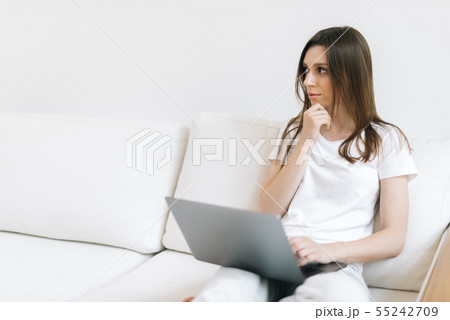 Close-up portrait of wondering girl looking away sitting at couch with laptop 55242709