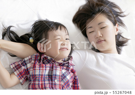 ベットに寝転びウィンクするイタズラ顔の幼い女の子と母。幸福、家族、愛情、親子、育児イメージ ベットに寝転びウィンクするイタズラ顔の幼い女の子と母。幸福、家族、愛情、親子、育児イメージ 55267048