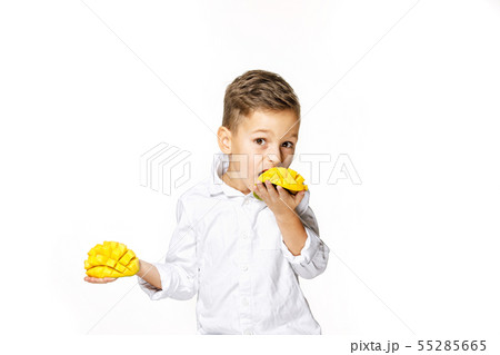 handsome boy in a white shirt is eating a mango 55285665