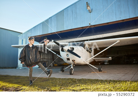 boy in large pilot jacket, playing with model airplane near aircraft hangar boy in large pilot jacket, playing with model airplane near aircraft hangar 55290372