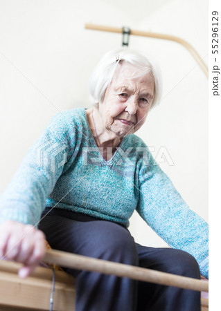 Elderly 96 years old woman exercising with a stick sitting on her bad. 55296129