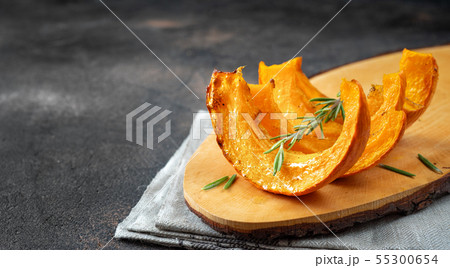 Slices of roasted pumpkin on wooden tray and dark background Slices of roasted pumpkin on wooden tray and dark background 55300654