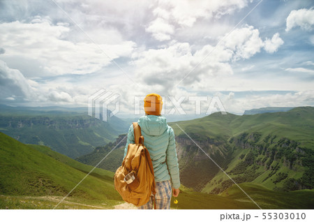 The view from the back of a tourist girl with a backpack is standing and looking at the mountain 55303010