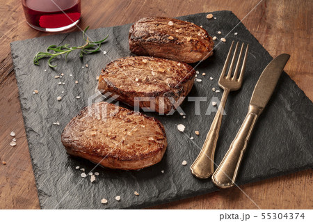 Sirloin or fillet beef steaks with salt, rosemary, and red wine on a black slate plate Sirloin or fillet beef steaks with salt, rosemary, and red wine on a black slate plate 55304374