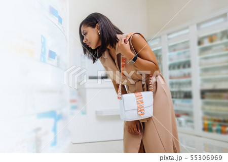 Pretty dark-skinned girl looking at shelf with medicine Pretty dark-skinned girl looking at shelf with medicine 55306969