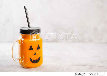 Halloween healthy pumpkin or carrot drink in the glass jar with scary face on a gray background 55311089