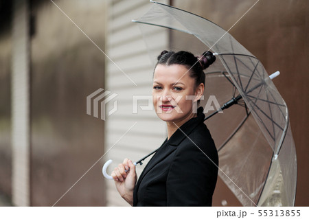 Young attractive woman in black jacket and blue jeans posing outdoor against background of building. 55313855