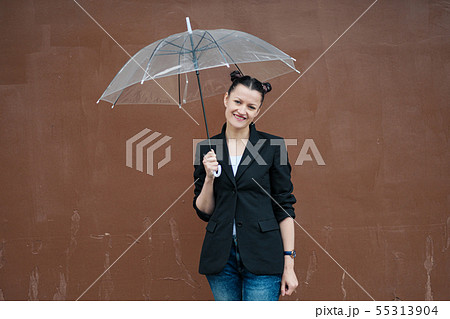 Young attractive woman in black jacket and blue jeans posing outdoor against background of building. 55313904