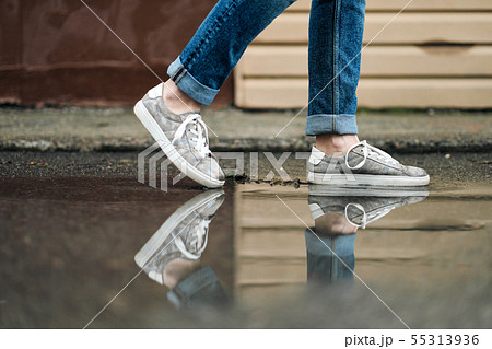 Close-up of feet in sneakers are walking through the puddles on the pavement. 55313936