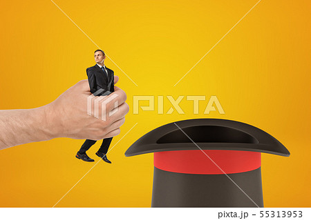 Man's hand holding tiny businessman and putting him in black top-hat on amber background with some Man's hand holding tiny businessman and putting him in black top-hat on amber background with some 55313953
