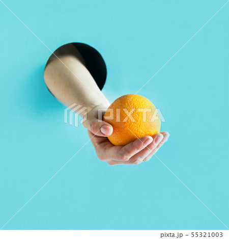 Female hand holding ripe orange in paper hole. 55321003