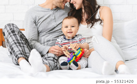 Sweet little baby smiling, sitting on bed with loving parents 55321420