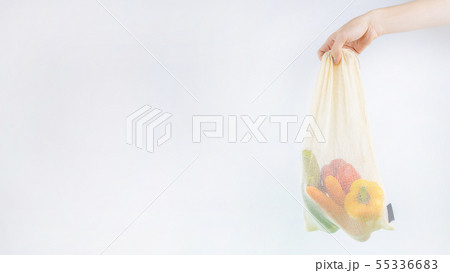 Hand holding net bag with vegetables inside. Hand holding net bag with vegetables inside. 55336683