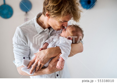A young father holding a newborn baby at home, kissing. A young father holding a newborn baby at home, kissing. 55338010