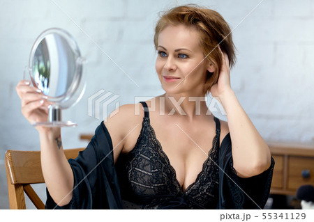 woman in a lace bodysuit and a dressing gown looks at herself in the mirror 55341129