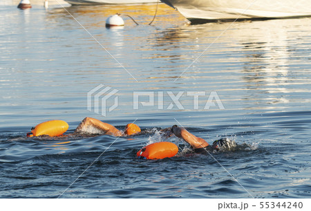 Two people swimming past moored boats with orange Two people swimming past moored boats with orange 55344240