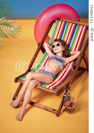 Girl wearing sunglasses and swimsuit sunbathing in rainbow deck chair 55348041
