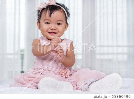 baby in pink dress on bed 55360496