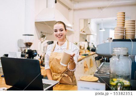 Caucasian smiling woman barista at the counter, suggesting a coffee cup. 55382351