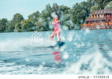 Smiling long-haired female wakeboarder sliding over the water 55388818