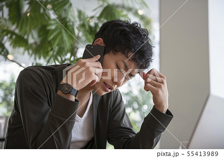 スマートフォンで通話をしながら顔をしかめる男性 55413989
