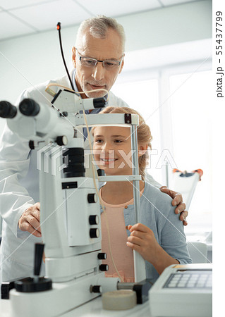 Grey-haired eye doctor wearing glasses standing near girl 55437799