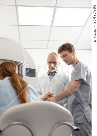 Dark-haired assistant of eye doctor helping him during examination 55437895