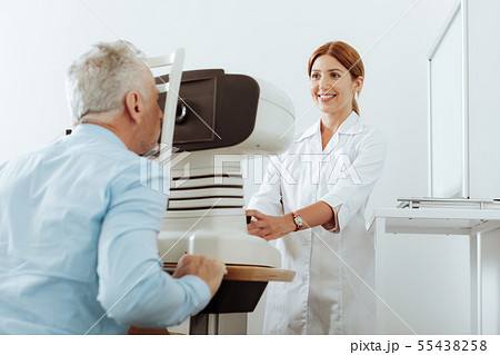 Red-haired eye doctor smiling while analyzing eye sight of patient Red-haired eye doctor smiling while analyzing eye sight of patient 55438258
