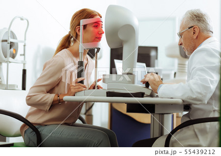 Young woman looking into special equipment for eyes diagnostics Young woman looking into special equipment for eyes diagnostics 55439212