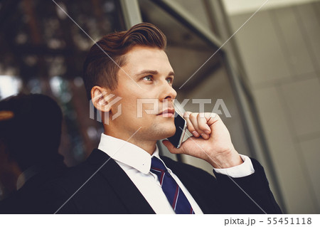 Close up of serious young man in black suit talking on the phone Close up of serious young man in black suit talking on the phone 55451118