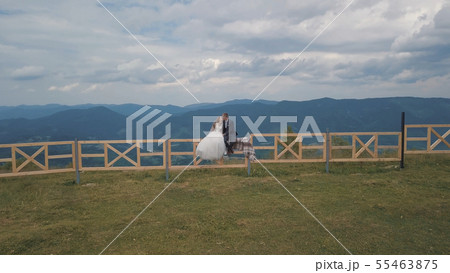 Groom with bride sit on the fence near mountain hills. Aerial drone shot 55463875