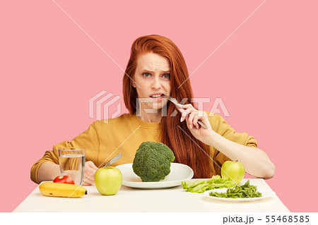 Vegetable diet. Sad dull woman holding broccoli on fork while making grimace 55468585