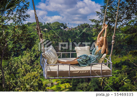 Young woman swinging in the jungle rainforest of Bali island, Indonesia. Swing in the tropics Young woman swinging in the jungle rainforest of Bali island, Indonesia. Swing in the tropics 55469335
