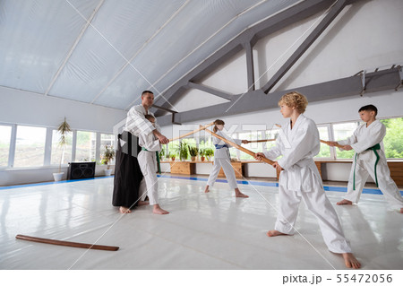 Children practicing aikido using jo standing near their trainer 55472056