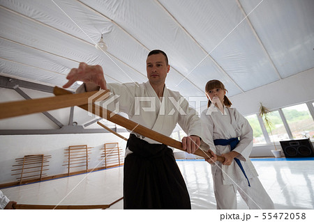 Trainer helping girl to use jo while practicing martial arts 55472058