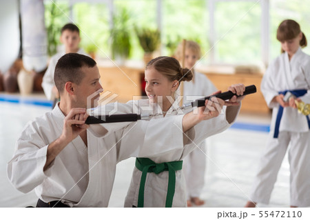 Dark-haired aikido trainer helping girl to use nunchucks Dark-haired aikido trainer helping girl to use nunchucks 55472110
