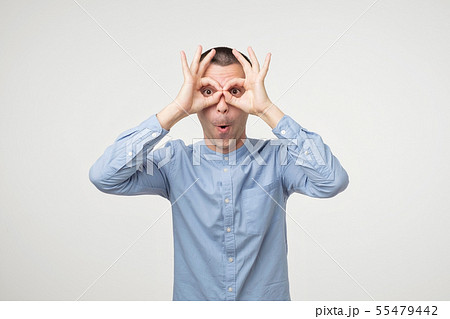 Young latin man showing owl sign with fingers. Young latin man showing owl sign with fingers. 55479442