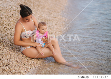 Young mother play with her baby girl on the beach by the sea. Mom and daughter in swimsuit Young mother play with her baby girl on the beach by the sea. Mom and daughter in swimsuit 55484937