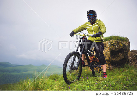 Side view of a man on a mountain bike standing on a rocky terrain and looking at a rock. The concept 55486728