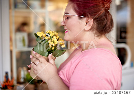 Young woman smelling blooming plant in flower pot 55487167