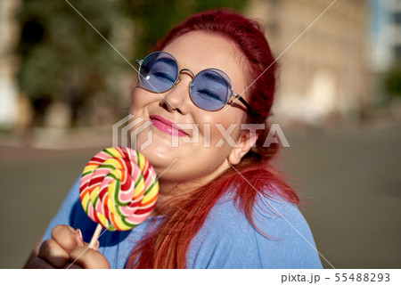 Fat young woman walking in city with lollipop Fat young woman walking in city with lollipop 55488293