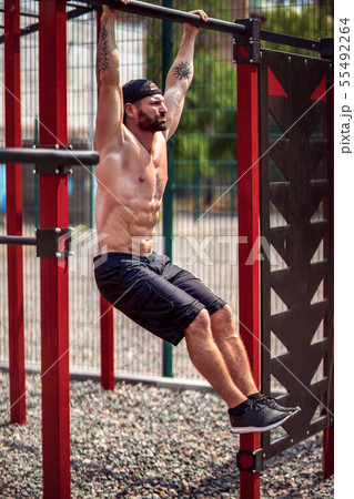Strong Muscular bearded man doing abdominal exercise on horizontal bar in summer park. fitness 55492264