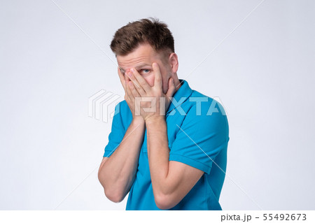 Man in blue t-shirt hiding cover face with hand Man in blue t-shirt hiding cover face with hand 55492673