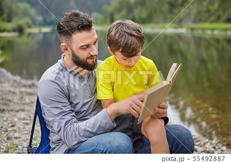 Family are reading book near river. Family are reading book near river. 55492887