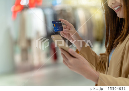 Closeup Asian woman using credit card with mobile for online shopping in department store over the clothes shop store background, technology money wallet and online payment concept, credit card mockup 55504051